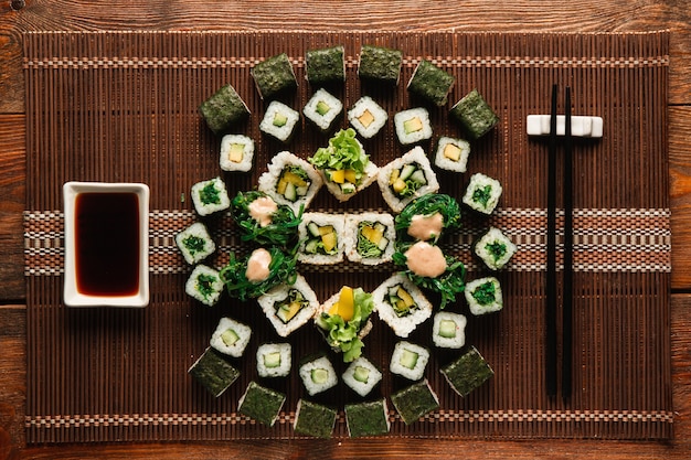 Grande ornamento de rolos de sushi vegetarianos servidos em uma esteira de palha marrom, plana. Cozinha tradicional japonesa, arte gastronômica, obra-prima da culinária.