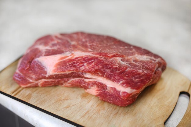 Grande pedaço de carne fresca na tábua de madeira na mesa de cozinha leve