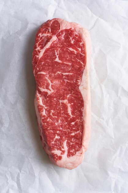 Foto grande pedaço inteiro de carne crua striploin em papel de pergaminho branco em fundo de artesanato