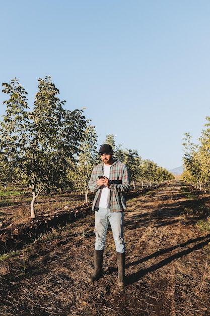 Grande plano de um jovem agricultor latino usando seu telefone ao lado da plantação de maçã Conceito agrícola