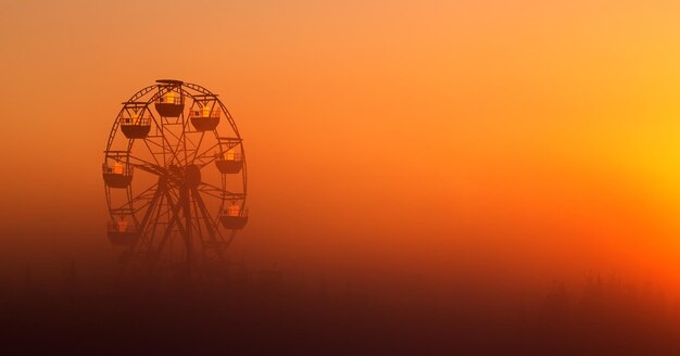 Grande roda-gigante branca em um parque nebuloso ao amanhecer.