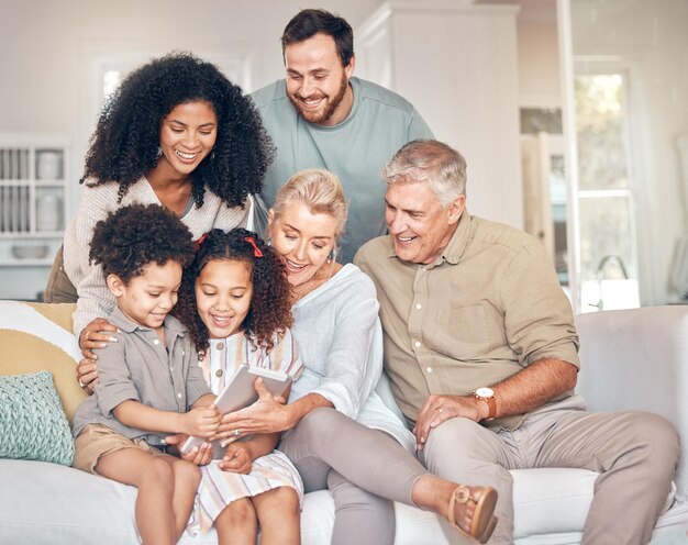 Grande tablet familiar e crianças em casa felizes e se unindo na sala de estar Tecnologia multirracial crianças e avós com pais no lounge transmitindo vídeo ou filme nas mídias sociais