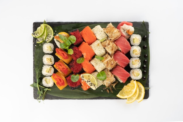 Grande variedade de maki de sushi variado feito de salmão, atum, ovas de camarão de peixe voador tobiko, arroz e sementes de gergelim em um planalto de pedra ardósia preta