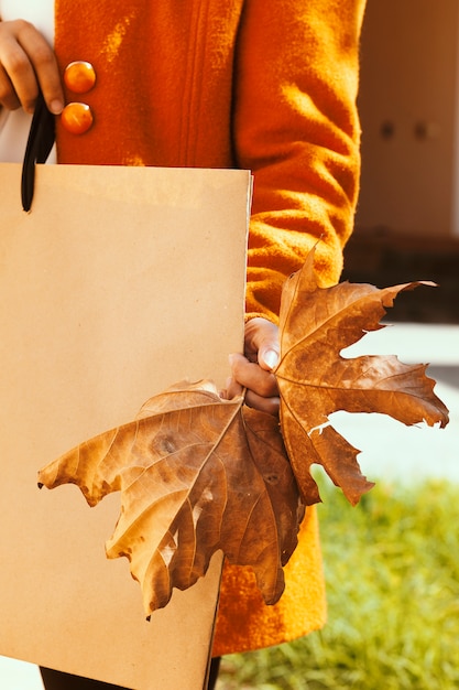 Grande venda de outono. mulher segurando uma folha de outono grande e sacola de compras. grande desconto de venda da temporada de outono