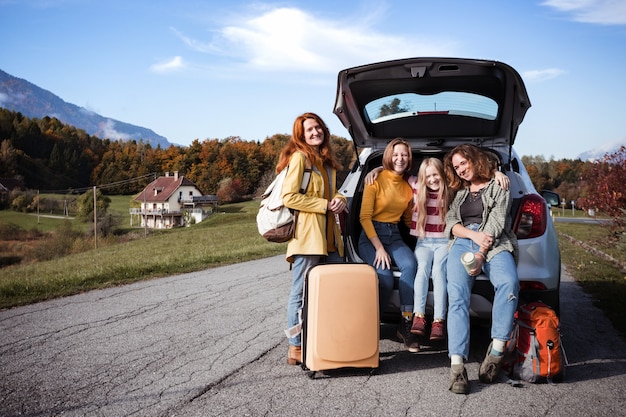 Grande viagem em família - meninas felizes viajam de carro. mamãe com filhas sentadas no porta-malas