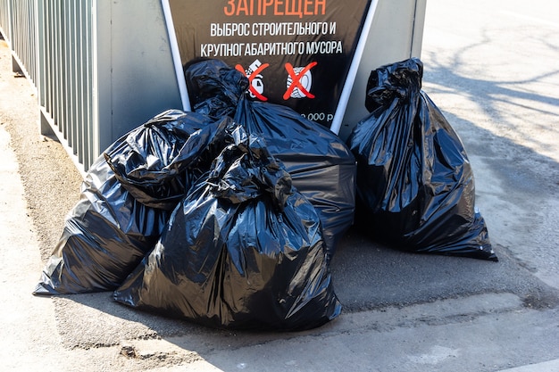 Grandes bolsas negras de basura cerca del contenedor de basura (inscripción en ruso: está PROHIBIDA LA LIBERACIÓN DE LA CONSTRUCCIÓN Y LA BASURA DE GRAN TAMAÑO)