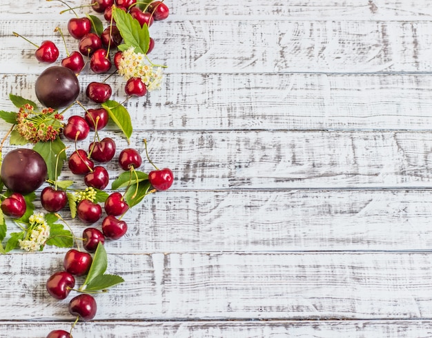 Grandes cerezas dulces y jugosas, ciruelas y uvas, follaje y flores sobre un fondo de madera