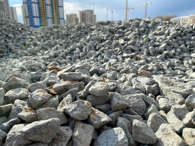 Grandes escombros de pedras cinzentas da construção de estradas industriais e uma visão de novos edifícios com guindastes