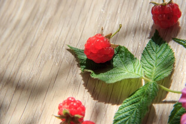 Foto grandes frambuesas de flores rosadas y hojas verdes en el fondo de madera