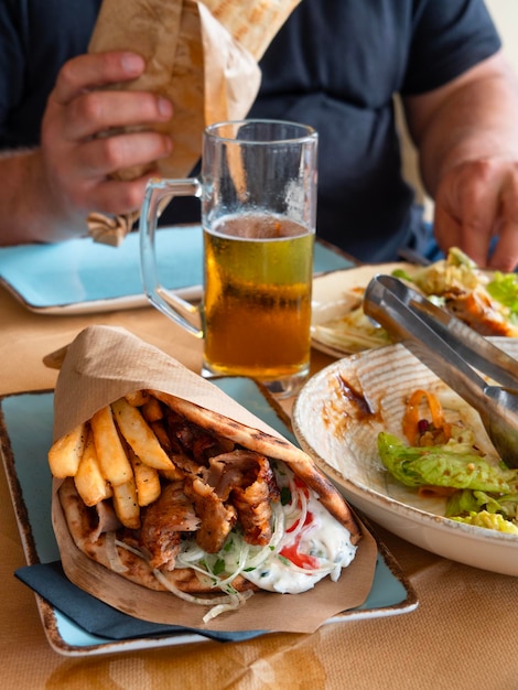 Grandes giros griegos con carne patatas fritas tomate cebolla en pita en la mano con un vaso de cerveza