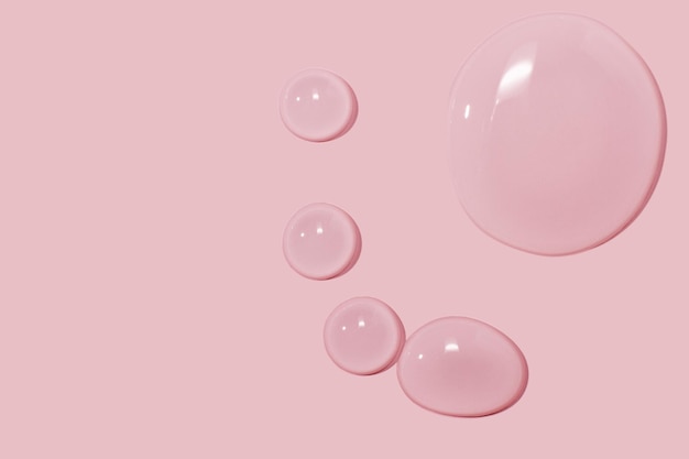 Grandes gotas de gel de água líquido de soro cosmético em um fundo rosa