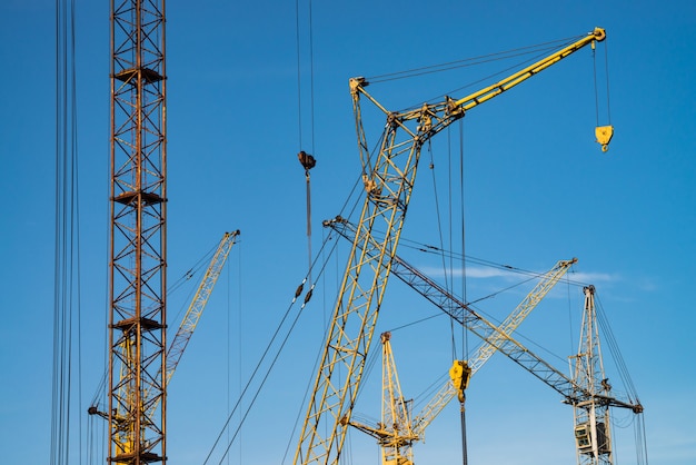 Grandes grúas torre contra el cielo azul. Imagen de fondo de primer plano de equipo de construcción con espacio de copia. Construir de ciudad.