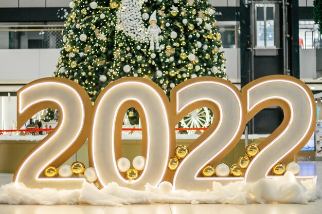 Grandes números brillantes 2022 en la sala en el piso con el telón de fondo del árbol de Navidad decorado. Feliz navidad y próspero año nuevo 2022