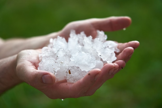 Grandes pedaços de gelo granizo na palma da sua mão. homem segurando um punhado de pedras de granizo grandes. consequências de anomalias naturais.