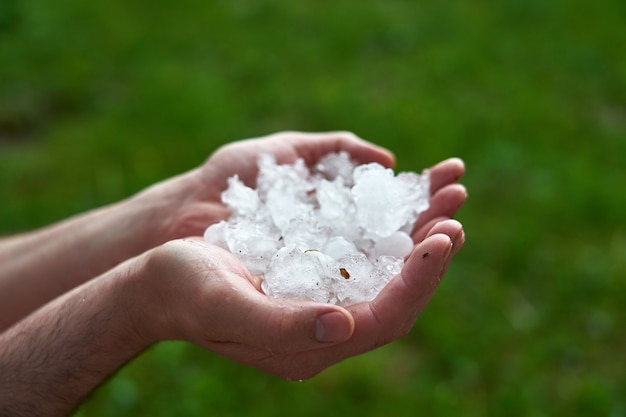 Grandes pedazos de hielo granizan en la palma de su mano. Hombre sosteniendo un puñado de granizo grande. consecuencias de anomalías naturales.