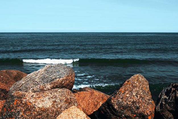 Foto grandes pedras ficam na praia em frente às ondas.