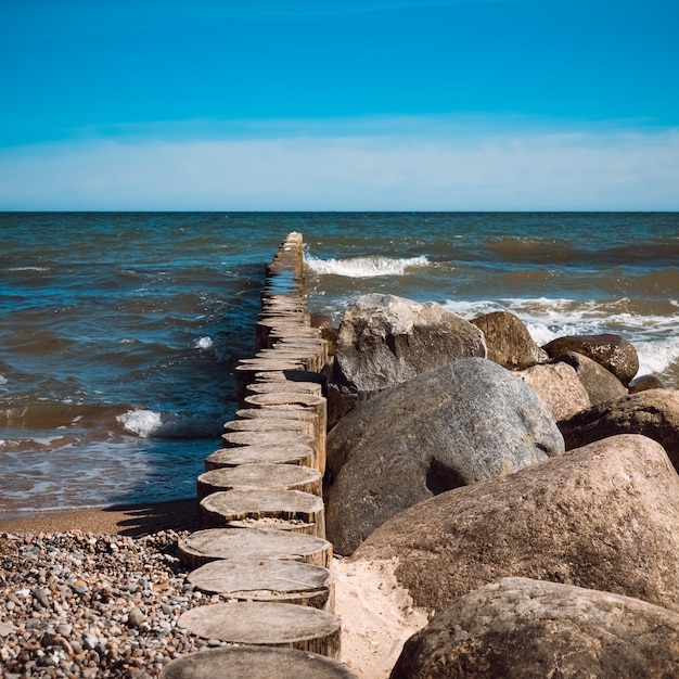 Grandes piedras se encuentran en la playa frente a las olas.