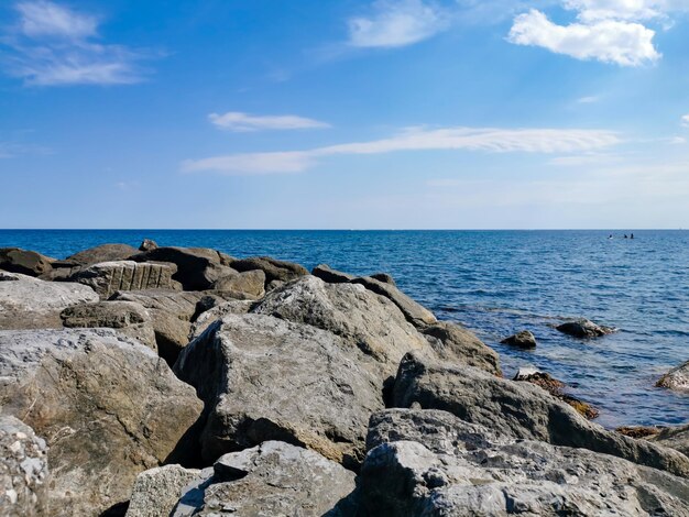 Grandes piedras en la orilla del mar en el fondo un cielo azul con nubes blancas. El mar de Liguria, Italia