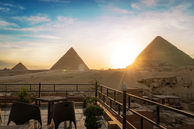 Grandes pirámides de Chephren Khafra y Keops Khufu y Mikerina Menkaura. Puesta de sol en la meseta de Giza. el sol se pone por debajo del horizonte. restaurante en la azotea en El Cairo con hermosa vista del hito. El Cairo, Egipto.