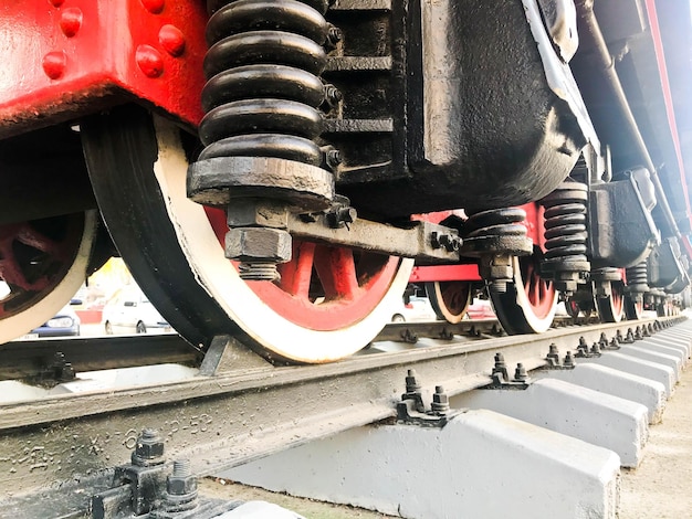 Grandes ruedas de hierro de un tren rojo y negro parado sobre rieles y elementos de suspensión con resortes