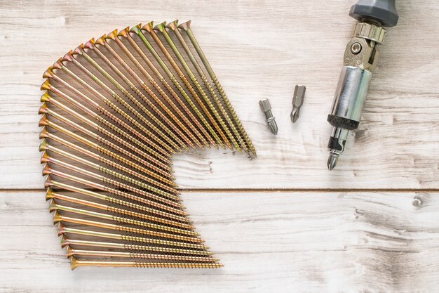 Grandes tornillos metálicos organizados en una fila con puntas de destornillador y destornillador sobre fondo de madera