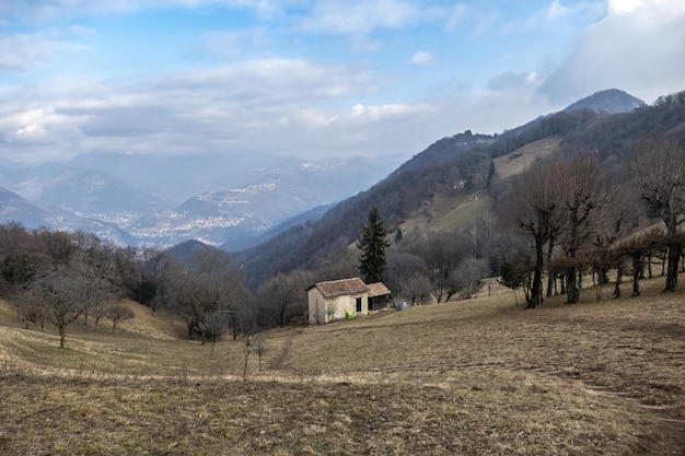 Granero en una colina cubierta de hierba y árboles desnudos bajo un cielo azul nublado en el campo