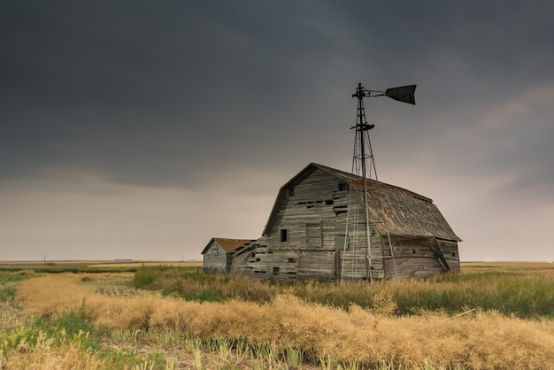 Granero, compartimientos y molino de viento de la vendimia bajo cielos oscuros siniestros en Saskatchewan, Canadá