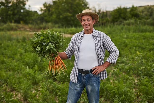 Granjero alegre con zanahorias frescas en campo