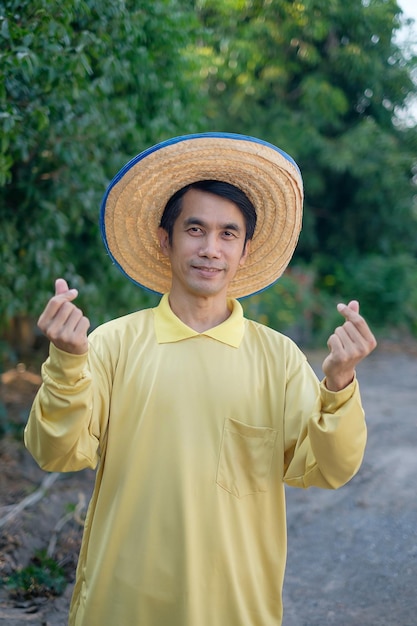 El granjero asiático usa una camisa amarilla, sonríe y presenta un mini dedo del corazón o una tarjeta de tenencia.