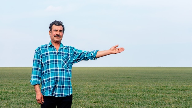 Granjero experimentado y confiado se encuentra en su campo con la mano extendida.