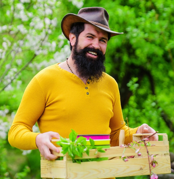 Granjero feliz en el jardín de primavera. Hombre barbudo con caja. Granja ecológica. Trabajo de jardinero.