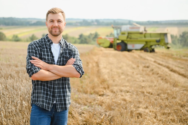 Granjero feliz de pie con orgullo en un campo Conductor de cosechadora va a cosechar una rica cosecha de trigo Agrónomo con camisa de franela mirando a la cámara en una tierra de cultivo