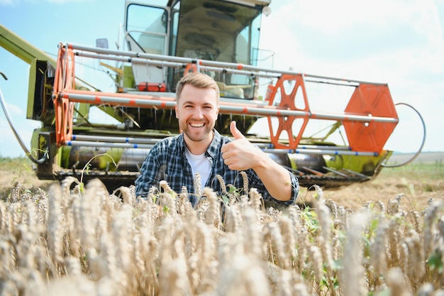 Granjero feliz de pie con orgullo en un campo Conductor de cosechadora va a cosechar una rica cosecha de trigo Agrónomo con camisa de franela mirando a la cámara en una tierra de cultivo