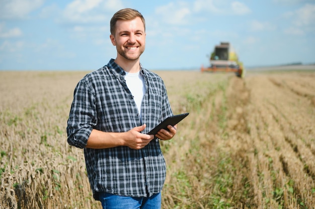 Granjero feliz de pie con orgullo en un campo Conductor de cosechadora va a cosechar una rica cosecha de trigo Agrónomo con camisa de franela mirando a la cámara en una tierra de cultivo