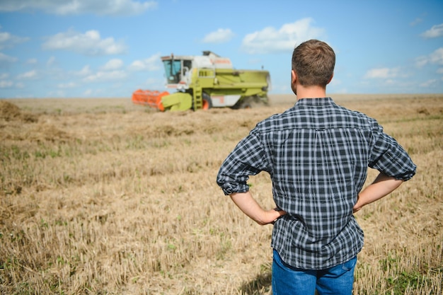 Granjero feliz de pie con orgullo en un campo Conductor de cosechadora va a cosechar una rica cosecha de trigo Agrónomo con camisa de franela mirando a la cámara en una tierra de cultivo