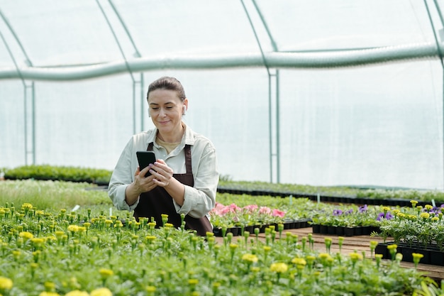 Granjero feliz con smartphone viendo videos de jardinería en línea