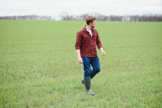 Granjero guapo Joven caminando en campo verde Agricultura de primavera