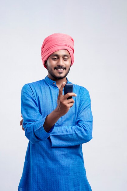Granjero indio joven que usa el teléfono móvil sobre el fondo blanco.