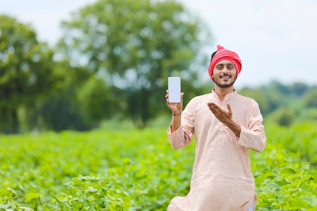 Granjero indio que muestra la pantalla del teléfono inteligente en el campo de la agricultura