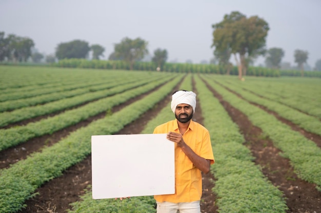 Granjero indio que muestra el tablero blanco en campo agrícola