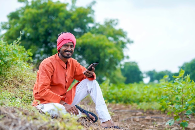 Granjero indio que usa un teléfono inteligente en el campo agrícola