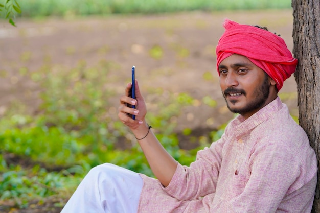 Granjero indio sentado en el campo de la agricultura y con smartphone.