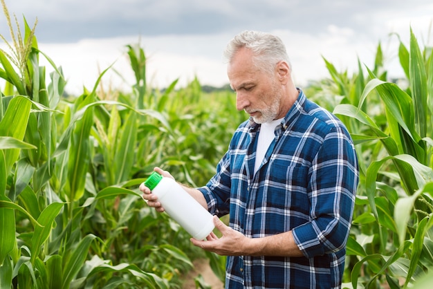 Granjero de mediana edad en un campo sosteniendo una botella con fertilizantes químicos