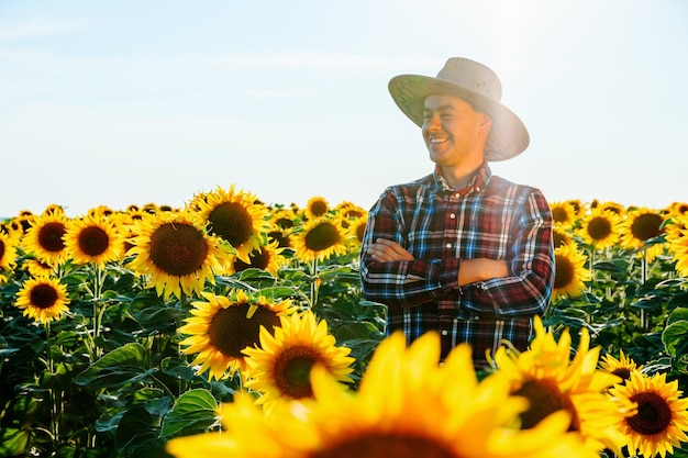 Un granjero satisfecho con un sombrero se para en un campo con girasoles al atardecer