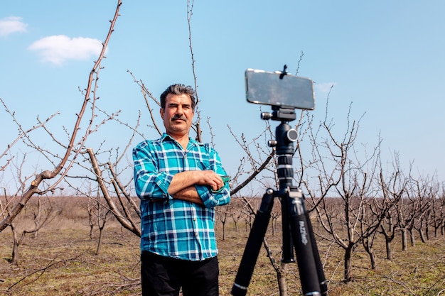 Granjero senior en el huerto, primavera, grabando contenido para el vlog del blog de estilo de vida,