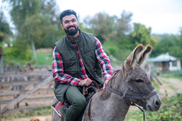 Un granjero sentado en un burro en una granja.