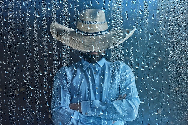 granjero con sombrero de paja detrás de gotas de lluvia de vidrio, clima estacional del salvaje oeste de América