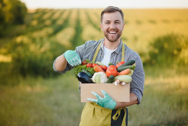 Granjero sosteniendo una caja de verduras biológicas en la granja Hombre feliz mostrando una caja de verduras cosechadas