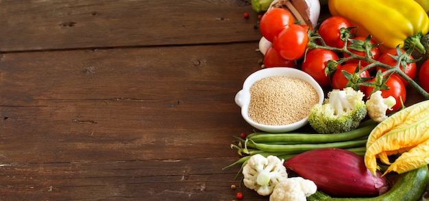 Grano de amaranto crudo en un recipiente y verduras en una mesa de madera de cerca con espacio de copia