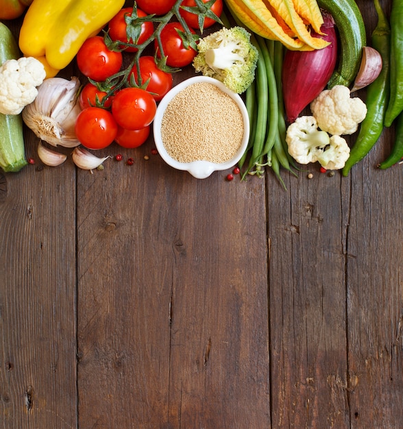 Grano de amaranto crudo en un recipiente y verduras sobre madera